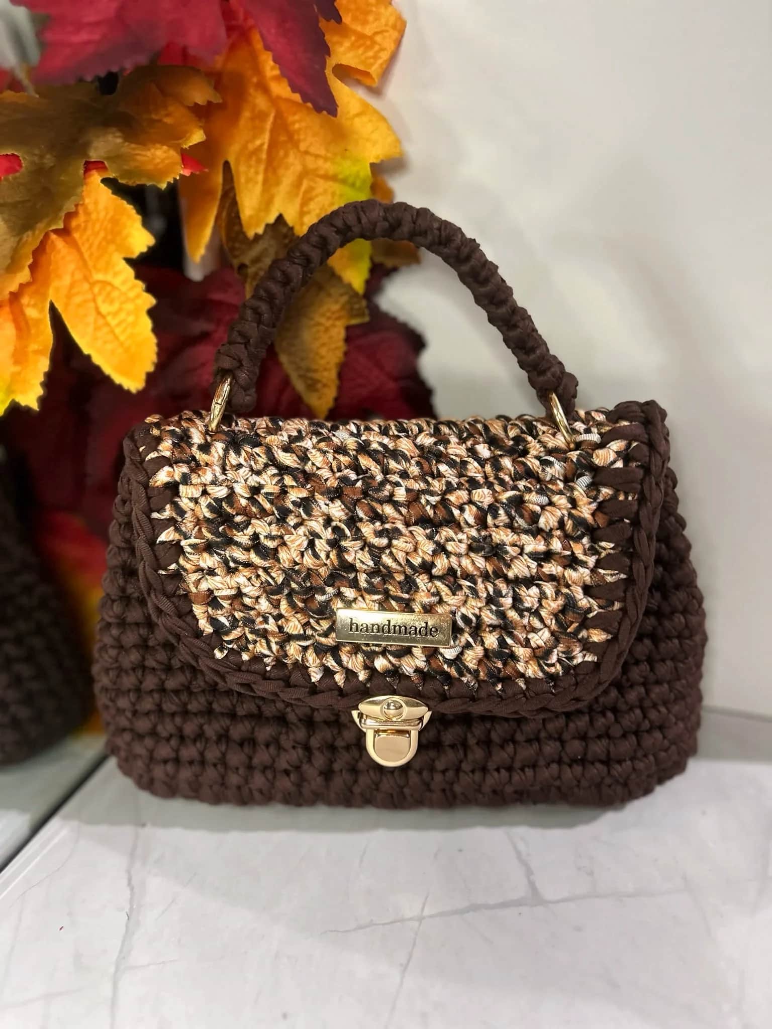 Brown crochet mini satchel with a top handle, patterned flap and gold clasp