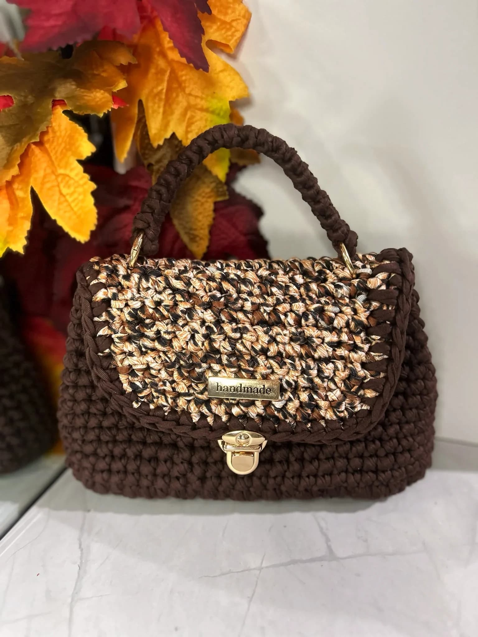 Brown crochet mini satchel with a top handle, patterned flap and gold clasp