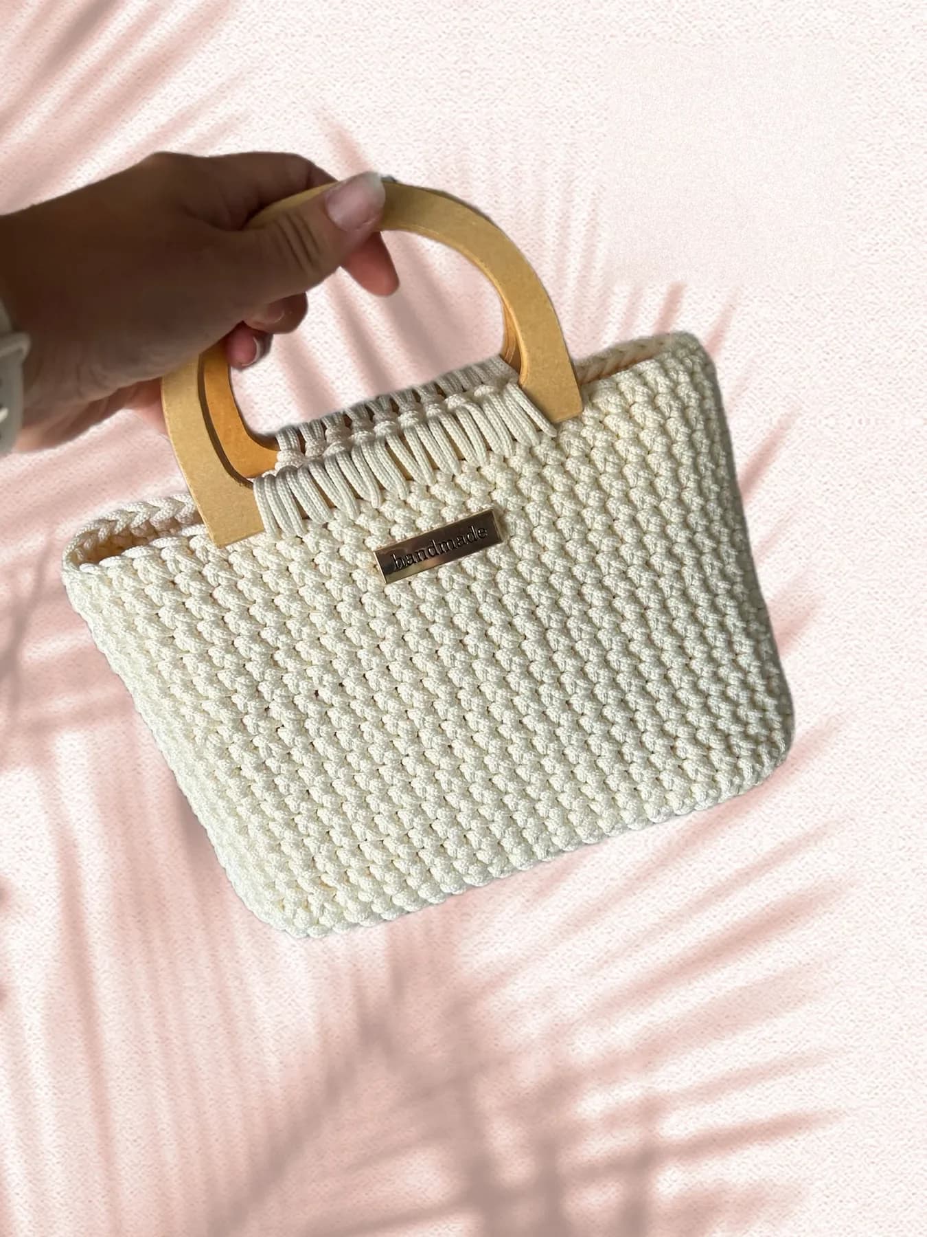 A small cream crochet tote with wooden handles, held up by one hand